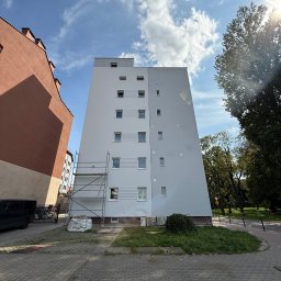 Halbud Taras Halats - Wysoki budynek po renowacji elewacji, widoczne rusztowania i worki z materiałami budowlanymi. Słoneczny dzień, błękitne niebo z chmurami.