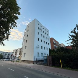 Halbud Taras Halats - Wysoki budynek po renowacji elewacji, z podnośnikiem koszowym przy ścianie. Widok z dołu, błękitne niebo w tle. Biała, odświeżona fasada.