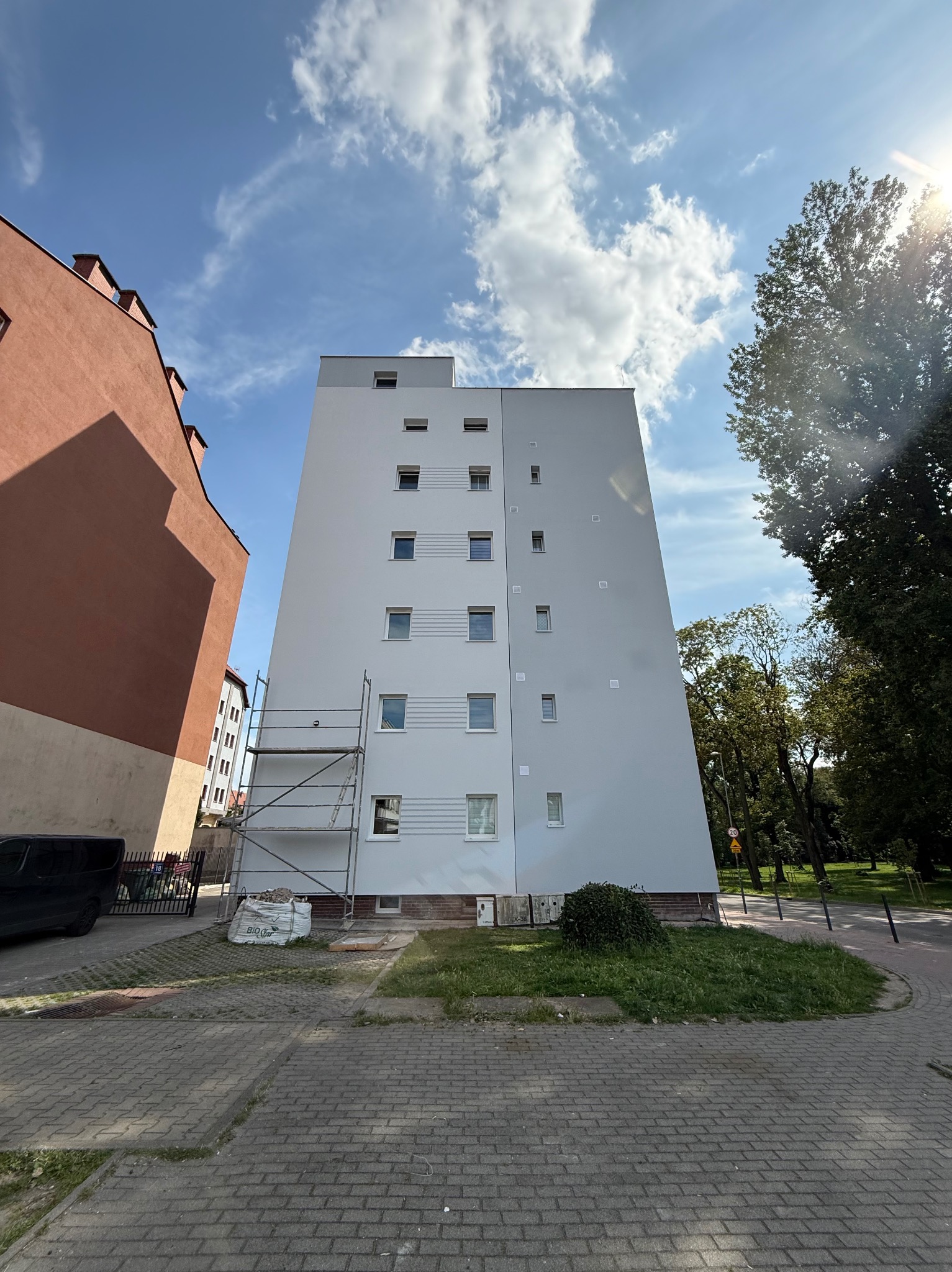 Wysoki budynek po renowacji elewacji, widoczne rusztowania i worki z materiałami budowlanymi. Słoneczny dzień, błękitne niebo z chmurami.