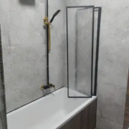 Nowoczesna łazienka: biała wanna z czarną armaturą i szklanym parawanem, szare płytki na ścianach i podłodze. Minimalistyczny design z akcentami złota.