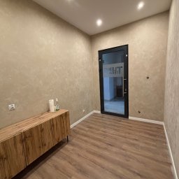 SEK-MAR SP.ZO.O. - Wnętrze po odświeżeniu: drewnopodobne panele, ściany z efektem dekoracyjnym, drewniana komoda i czarne drzwi z przeszkleniem. Nowoczesny minimalizm.