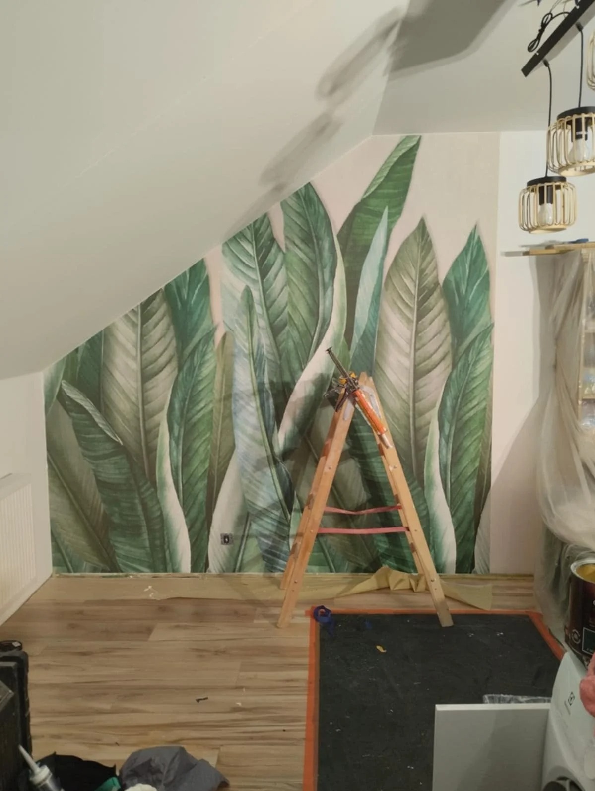 Ściana z motywem liści w Gdyni, drabina oparta o ścianę, widoczne narzędzia malarskie. Realizacja z zakresu dekoracji wnętrz.