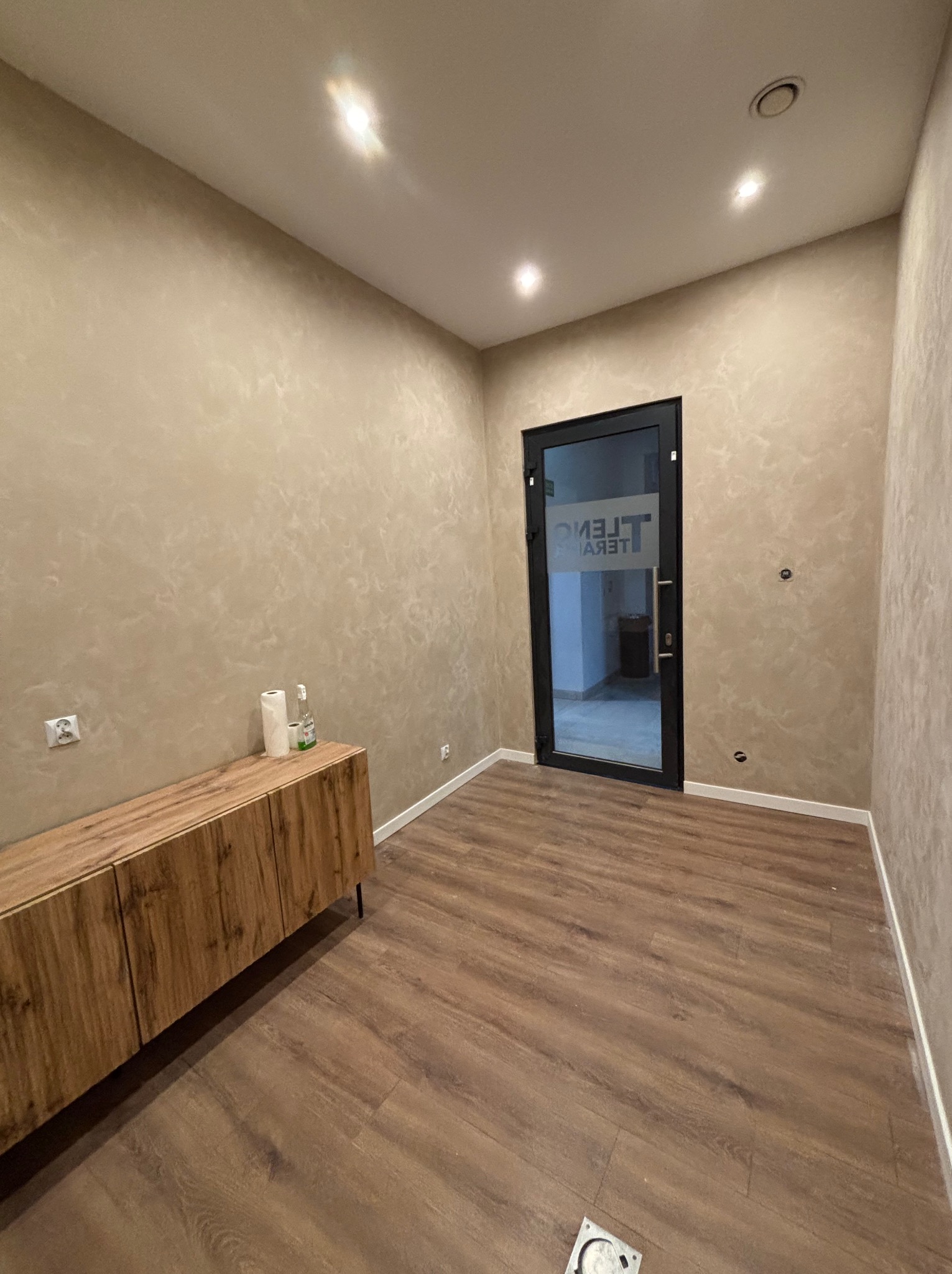 Wnętrze po odświeżeniu: drewnopodobne panele, ściany z efektem dekoracyjnym, drewniana komoda i czarne drzwi z przeszkleniem. Nowoczesny minimalizm.