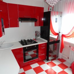 SK3D Serhii Khmel - Czerwono-biała kuchnia z błyszczącymi frontami, czarnym sprzętem AGD i podświetleniem. Uwagę przykuwają okiennice i wzorzysta podłoga.
