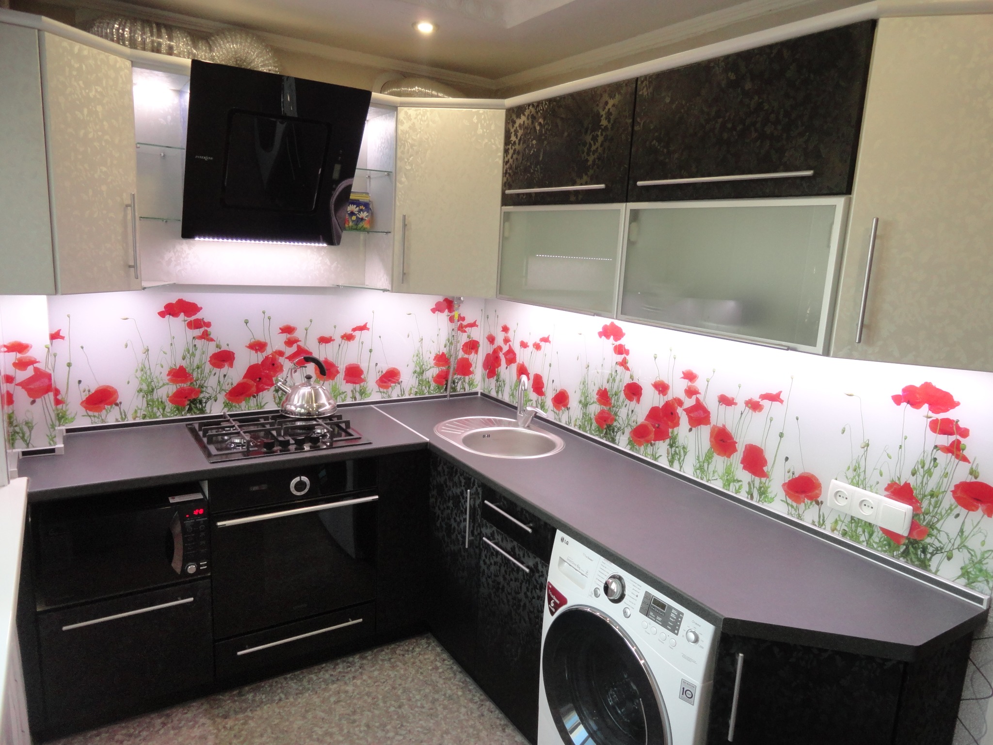 Nowoczesna kuchnia na wymiar z czarnymi blatami, szklanym panelem z motywem maków, podświetleniem LED i wbudowanymi sprzętami AGD, w tym pralką.