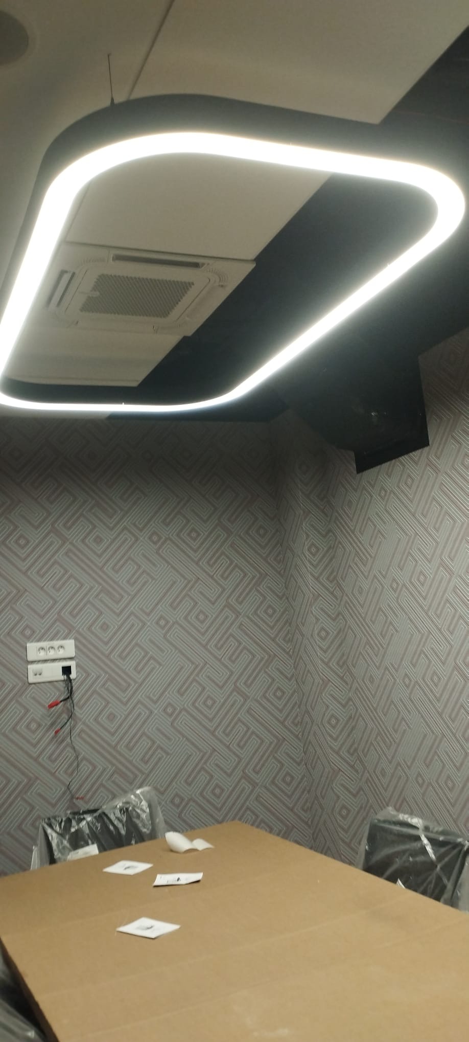 Nowoczesne oświetlenie LED w kształcie zaokrąglonego prostokąta, zamontowane na suficie podwieszanym w biurze z wzorzystą tapetą i klimatyzacją kasetonową.