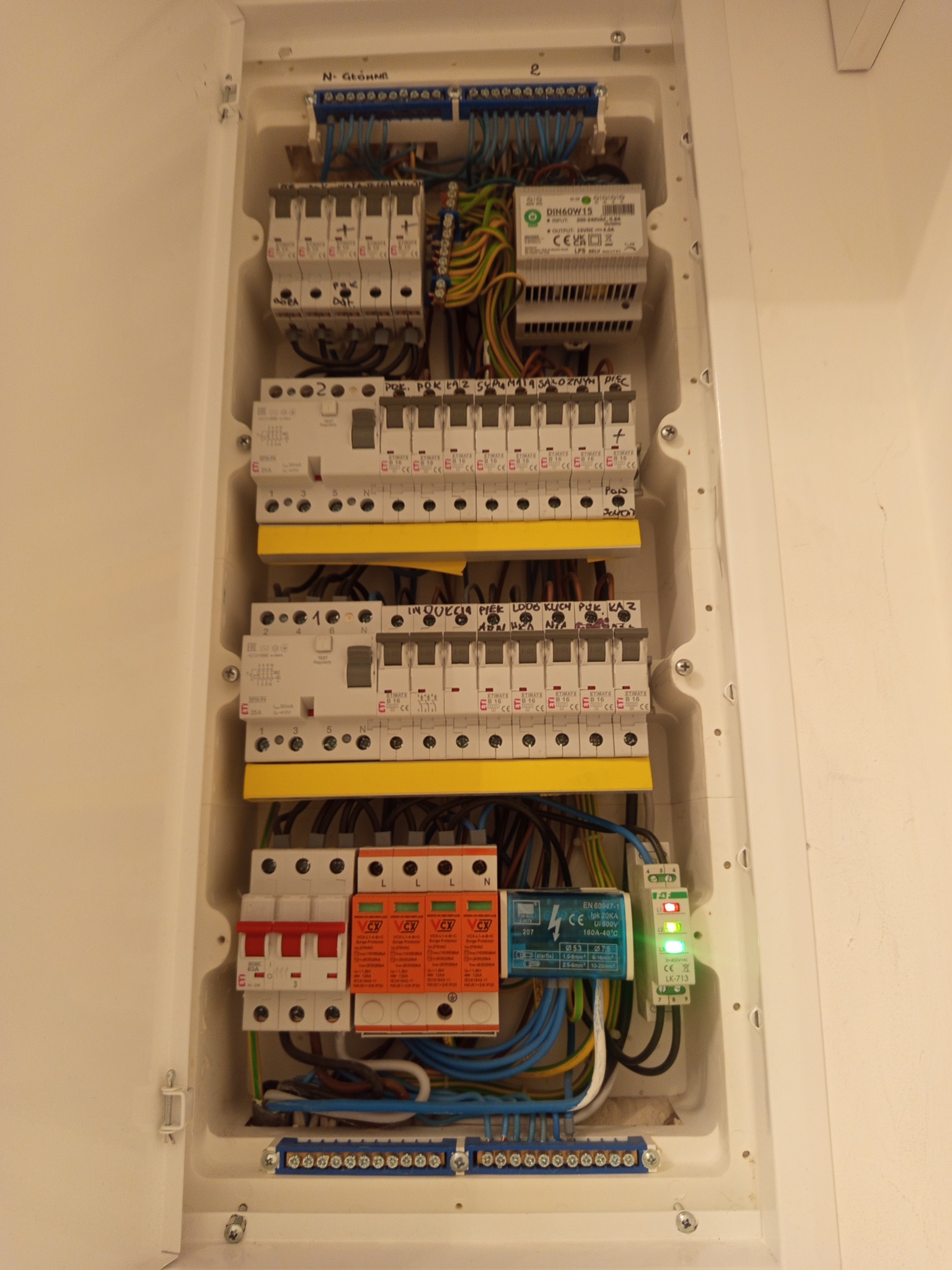 Rozdzielnica elektryczna z zabezpieczeniami, widoczne bezpieczniki, przewody i listwy zaciskowe w białej obudowie. Uporządkowany układ przewodów.