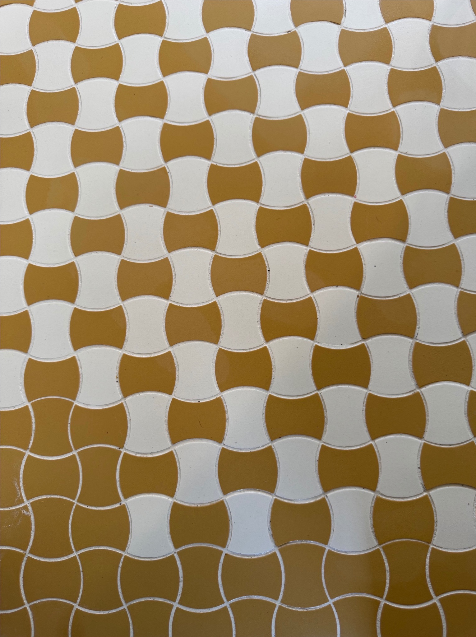Mozaika z białych i miodowych płytek w kształcie zaokrąglonych kwadratów, ułożonych naprzemiennie. Widok z góry, równomierne oświetlenie.