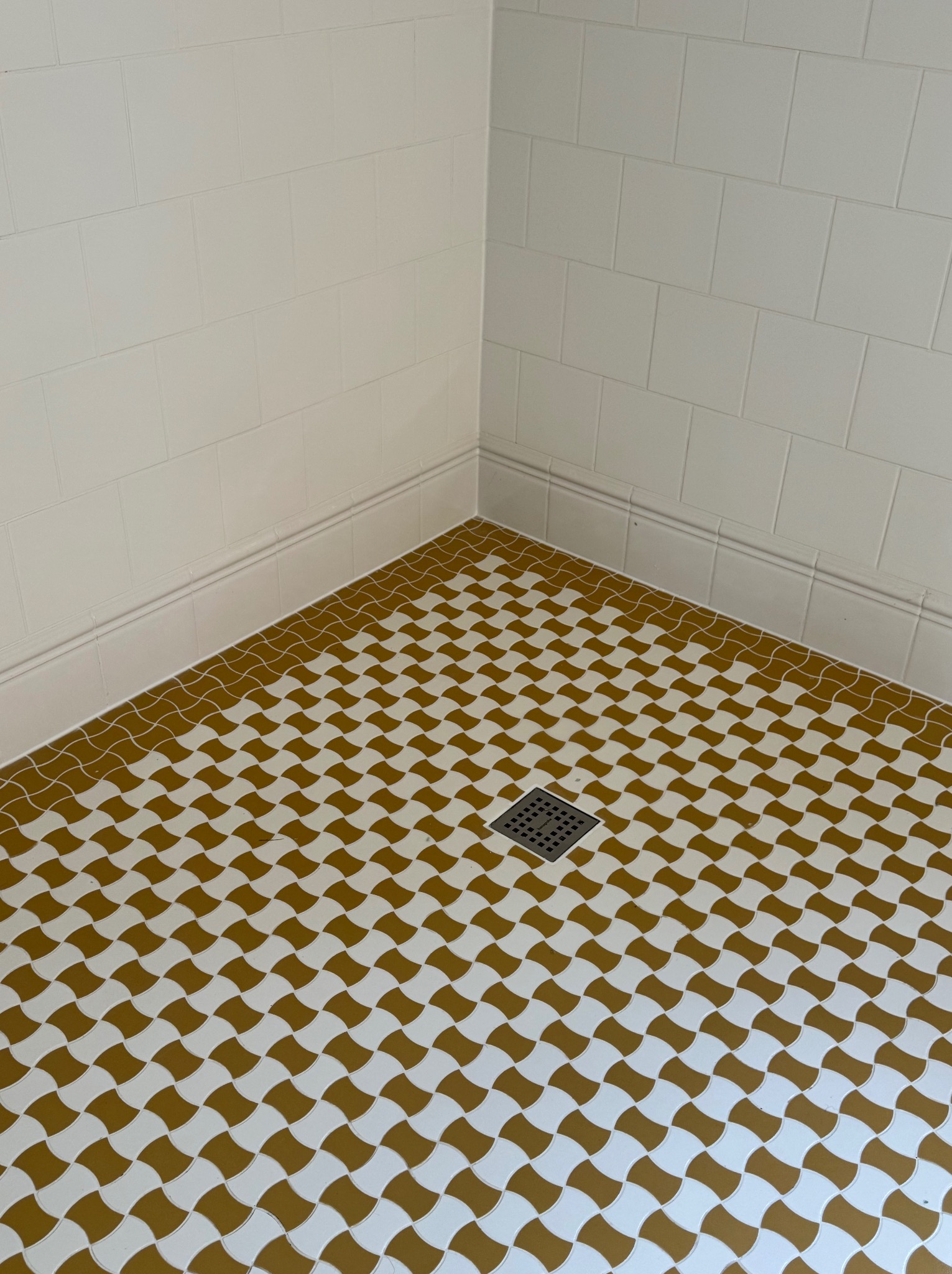 Wykończona łazienka z oryginalną, wzorzystą podłogą w odcieniach bieli i złota. Widoczny odpływ liniowy i białe, klasyczne płytki na ścianach.