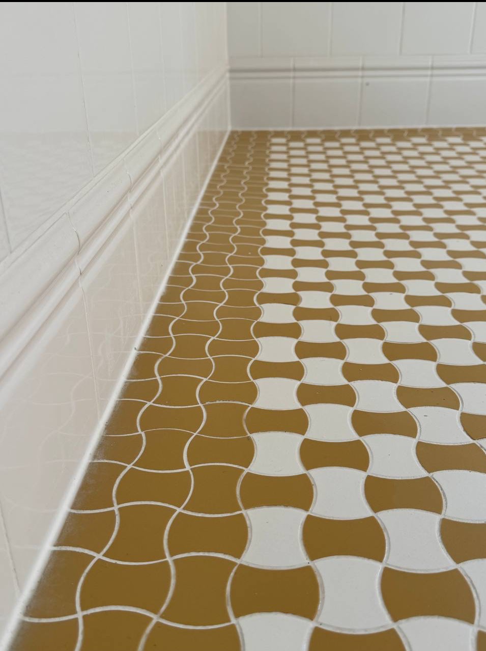 Ukończona podłoga w łazience z wzorem mozaiki w odcieniach bieli i brązu. Widoczne białe listwy przypodłogowe i płytki ścienne.