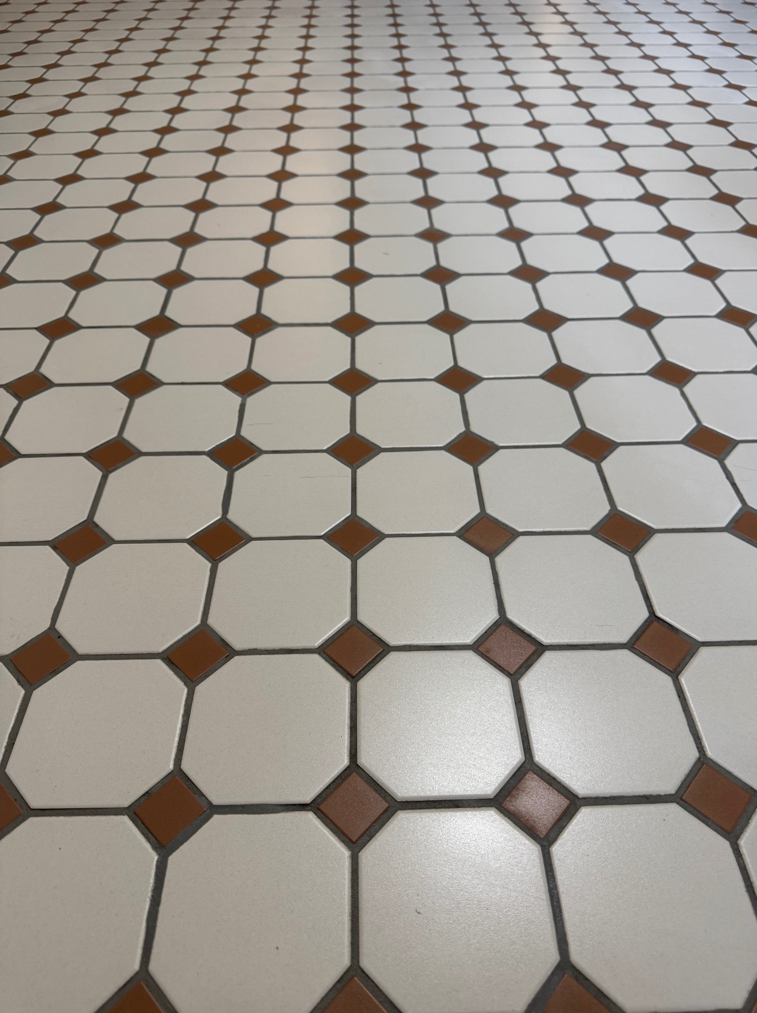 Ułożona podłoga z jasnych, ośmiokątnych płytek z brązowymi wstawkami w kształcie rombów. Widok z perspektywy podłogi, fuga w kolorze szarym.