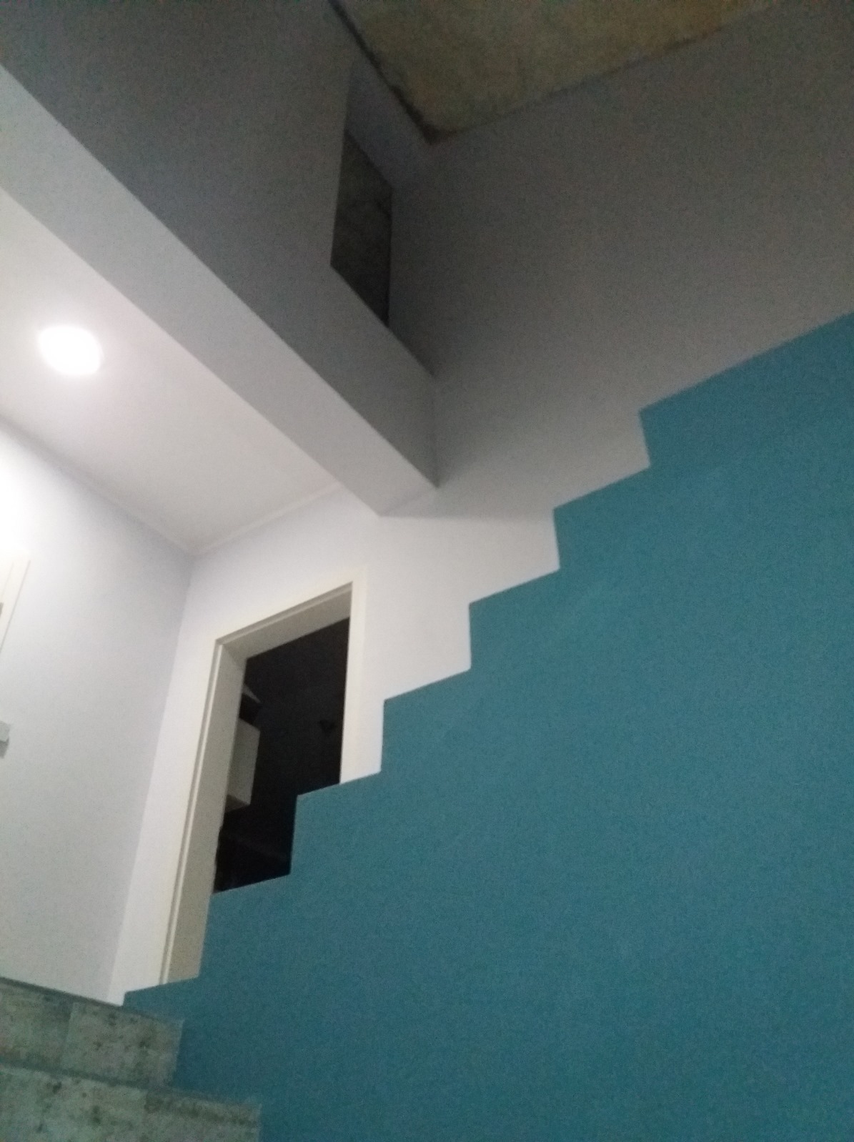 Błękitna ściana schodów z białymi akcentami w Herford. Widoczne drzwi i fragment sufitu. Nietypowe połączenie kolorów i kąt ujęcia.