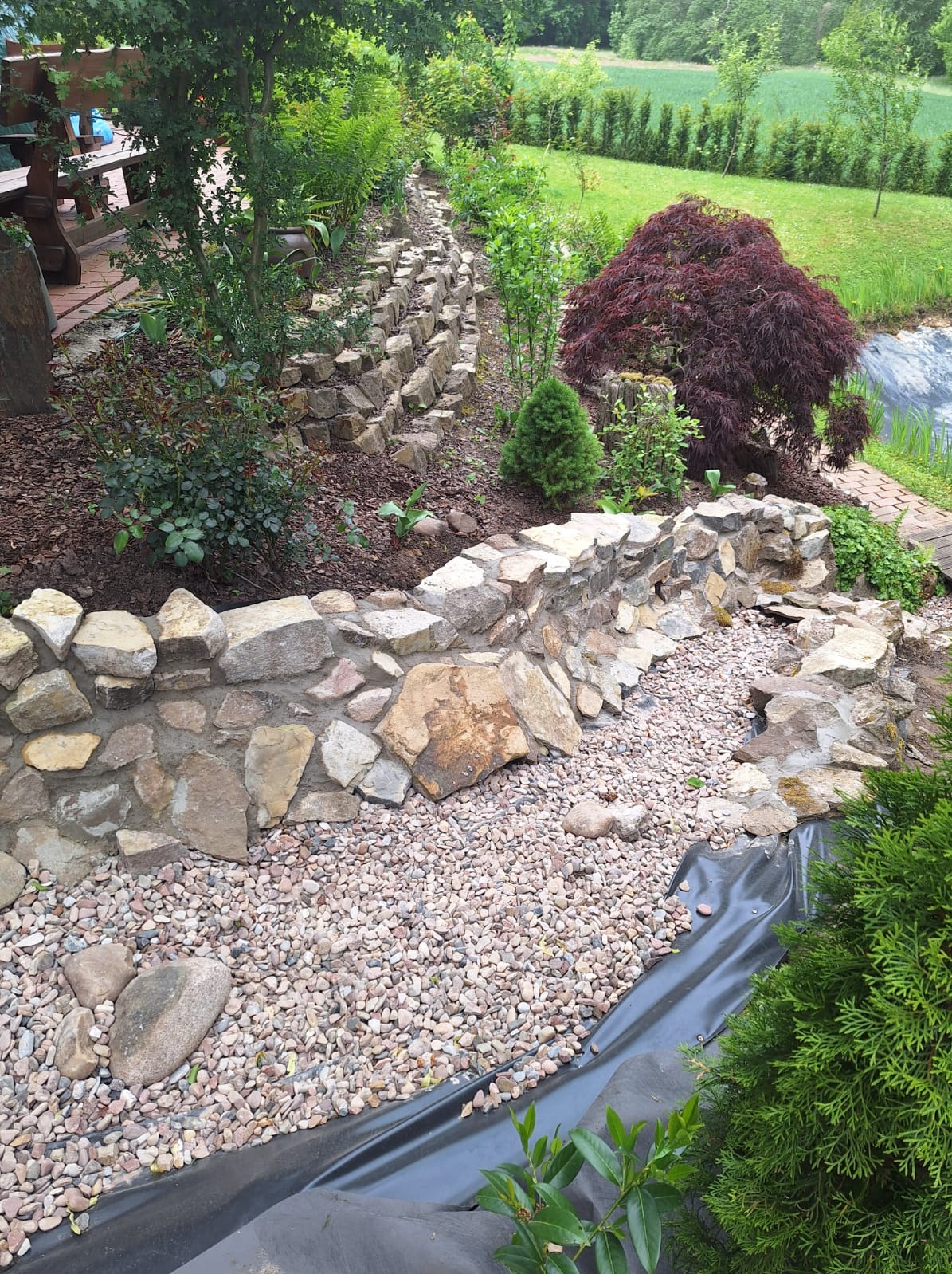 Ogród z kamienną kaskadą i ozdobnymi roślinami. Wyjątkowy element krajobrazu z użyciem kamienia i zieleni. Dekoracyjny mur oporowy z kamienia.