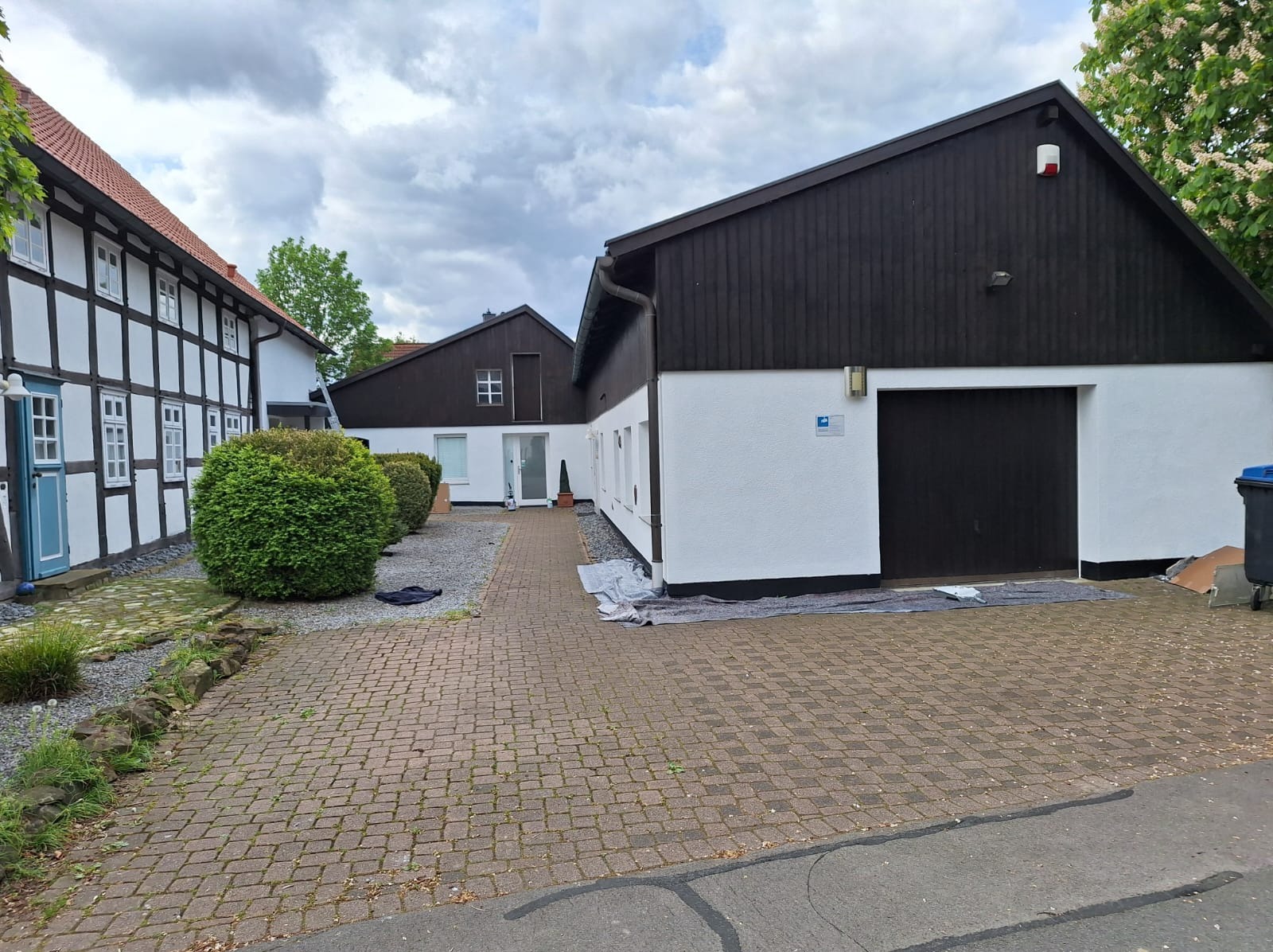 Biało-czarny budynek po renowacji z brązową bramą garażową, widok z zewnątrz na kostkę brukową i fragment ulicy.