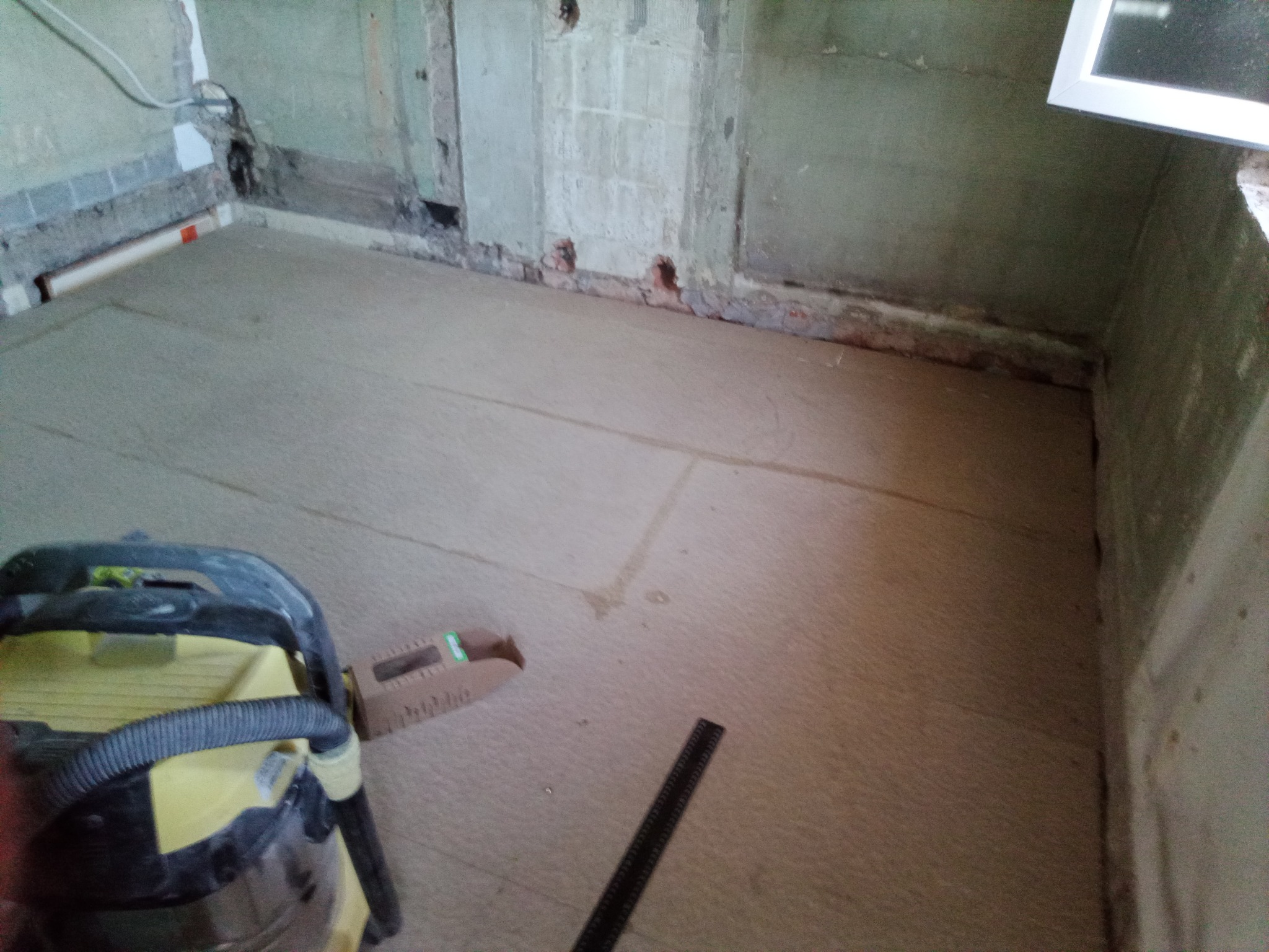 Przygotowanie podłoża w Herford: wyrównana podłoga w surowym wnętrzu, gotowa do dalszych prac wykończeniowych. Widoczny odkurzacz i narzędzia pomiarowe.