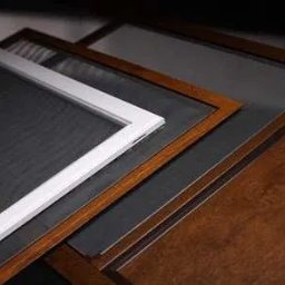 Adrian Kowalczyk - Różne ramki moskitier: biała aluminiowa, brązowa drewnopodobna i szara, ułożone warstwowo, ukazujące detale siatki i wykończenia. Ciemne tło.