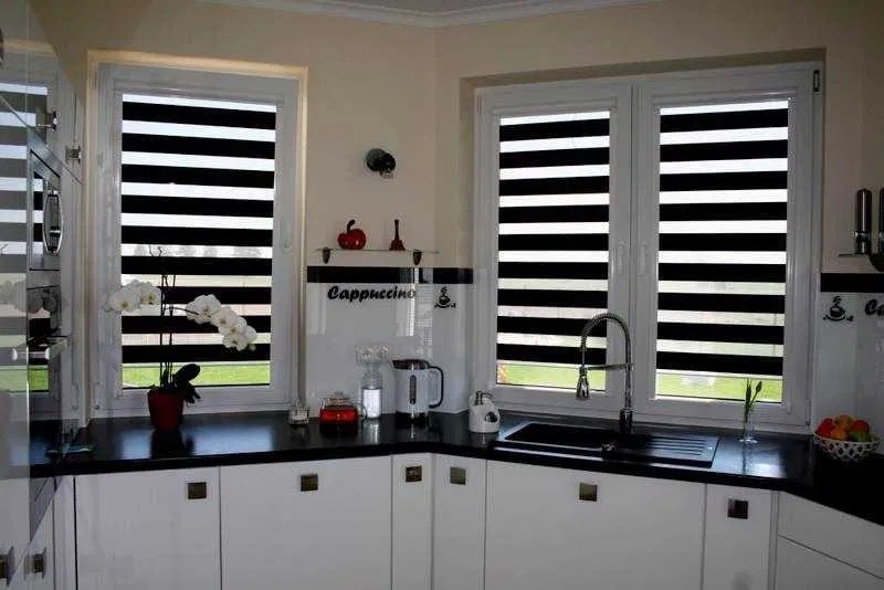Rolety dzień noc w kuchni we Wrocławiu. Dwie rolety w oknach, czarno-białe pasy, nowoczesny design. Widok na zewnątrz przez okno.