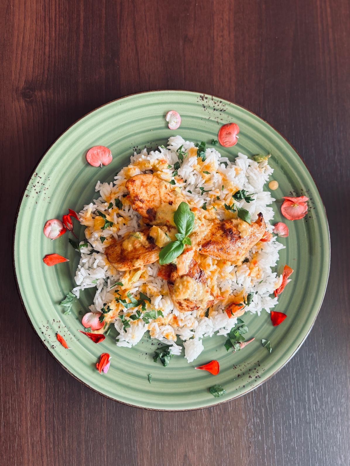 Danie z kurczaka w sosie, podane na ryżu z ziołami i jadalnymi kwiatami na zielonym talerzu, na ciemnym drewnianym stole. Elegancka prezentacja.
