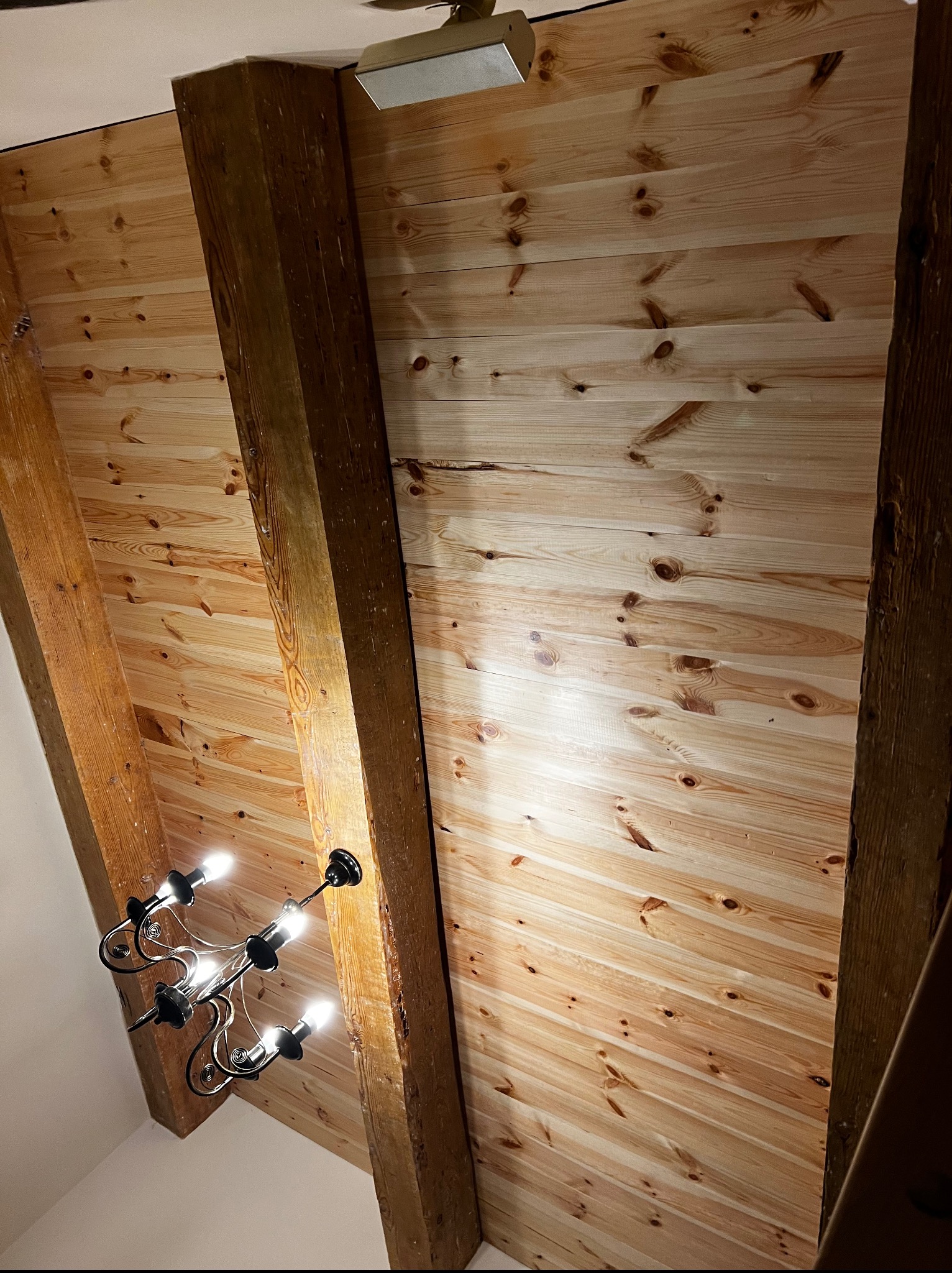 Drewniany sufit ze skośnymi belkami i ozdobnym żyrandolem. Widok z dołu, podkreślający strukturę drewna i oświetlenie.