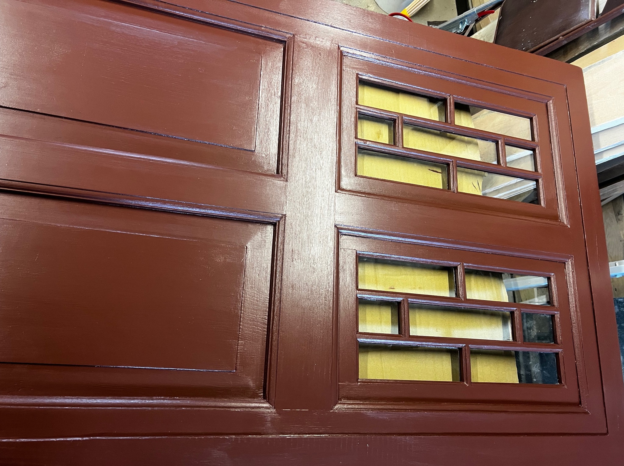 Odnowione, brązowe drzwi z szybkami po renowacji. Widoczne świeże malowanie i odświeżony wygląd. Detale stolarskie podkreślone nową warstwą farby.