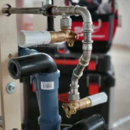 Złożony system rur z mosiężnymi zaworami i złączkami, widoczny na tle skrzynki narzędziowej, prezentuje instalację wodno-kanalizacyjną w trakcie montażu.