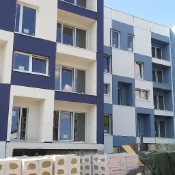 Paxon LTD - Nowoczesna elewacja budynku w szachownicę, z widocznymi rusztowaniami na sąsiednim budynku i materiałami izolacyjnymi u podstawy.