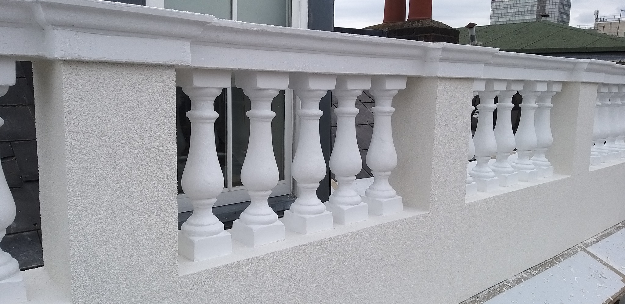 Biała balustrada z balaskami po renowacji elewacji w Świdnicy. Świeżo pomalowana, z widoczną fakturą tynku i detalami architektonicznymi. Tło stanowią okna i dach budynku.