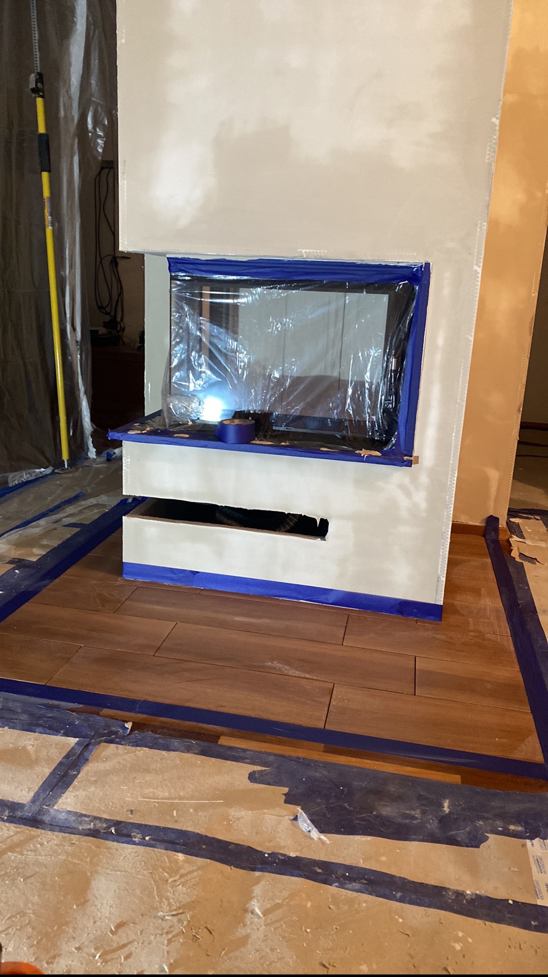 Remont kominka w Limanowej: zabezpieczony folią otwór, świeżo pomalowana ściana, podłoga wyłożona płytkami i zabezpieczona taśmą malarską. Detal z etapu prac.