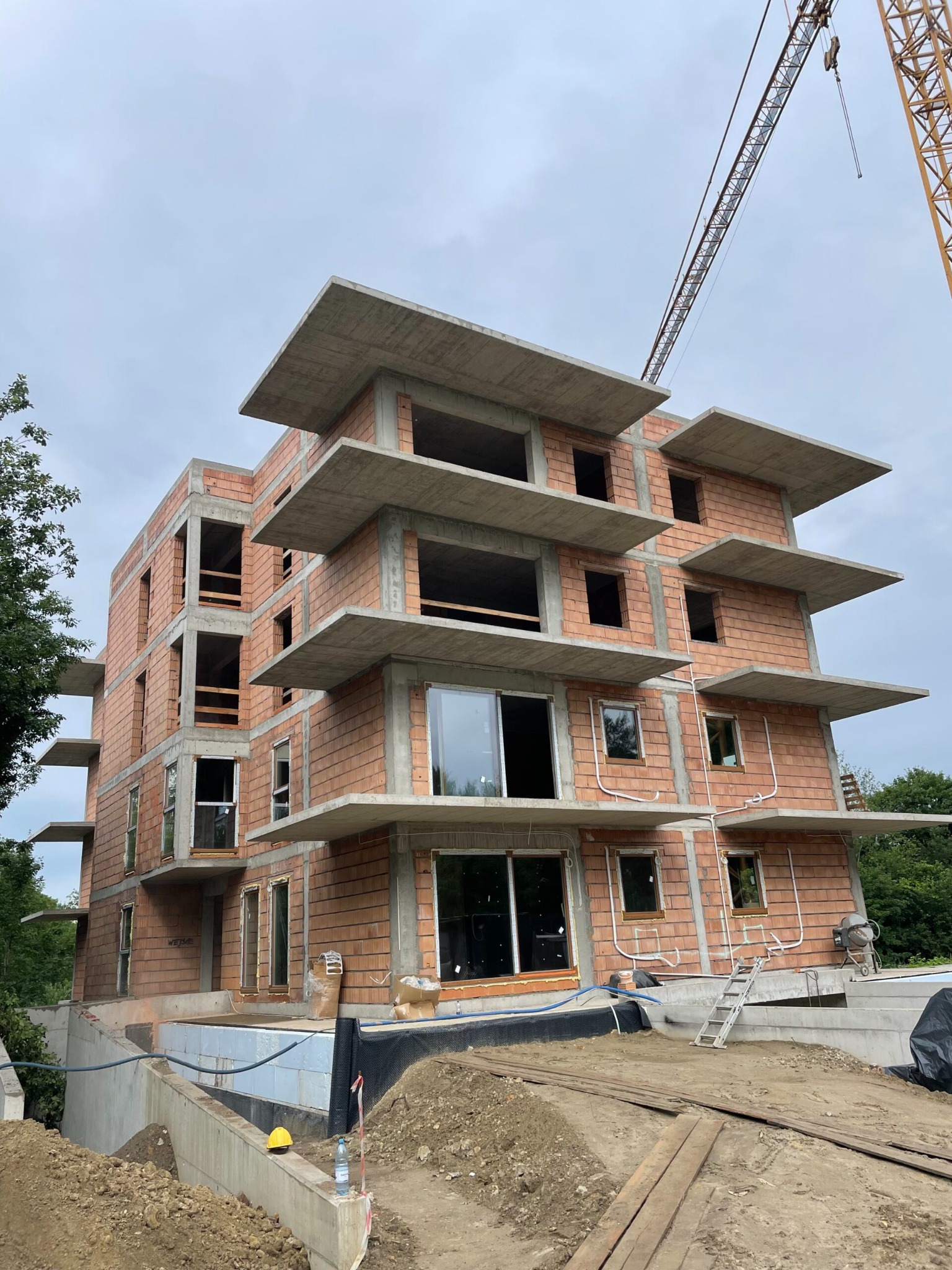 Wielopiętrowy budynek mieszkalny w trakcie budowy, z widocznymi elementami konstrukcyjnymi i dźwigiem w tle, Sosnowiec. Budowa w toku, cegła i beton.