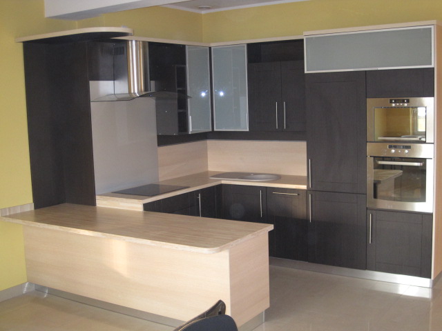 Nowoczesna kuchnia z ciemnymi szafkami, jasnym blatem i wyspą kuchenną z blatem w kolorze drewna, okap ze stali nierdzewnej, piekarnik w zabudowie.