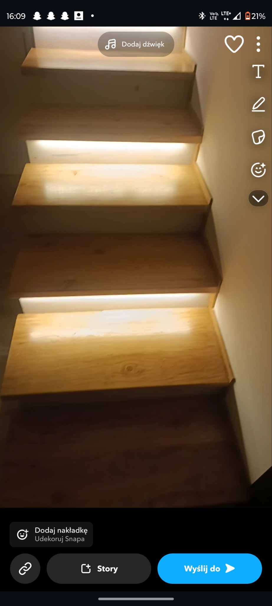 Drewniane schody z subtelnym oświetleniem LED pod każdym stopniem, tworzącym ciepłą, dekoracyjną iluminację wzdłuż ściany. Widok z dołu, skupiony na detalach.