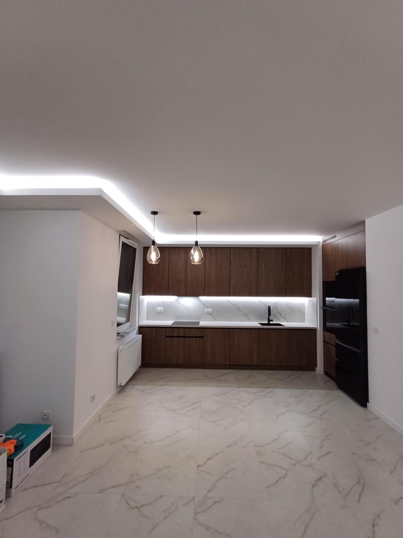 Nowoczesna kuchnia z drewnianymi szafkami, marmurowym blatem i podświetleniem LED podszafkowym oraz sufitowym. Dwie wiszące lampy nad blatem. Minimalistyczny design.