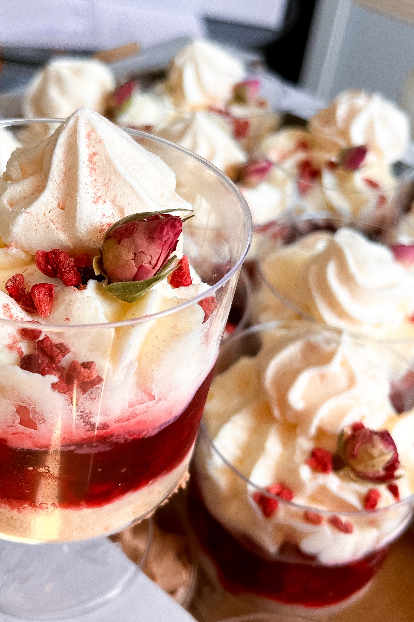 Deser w przezroczystym pucharku: warstwy kremu, galaretki i biszkoptu, udekorowany suszoną różą i malinami. Słodka kompozycja, idealna na przyjęcie.