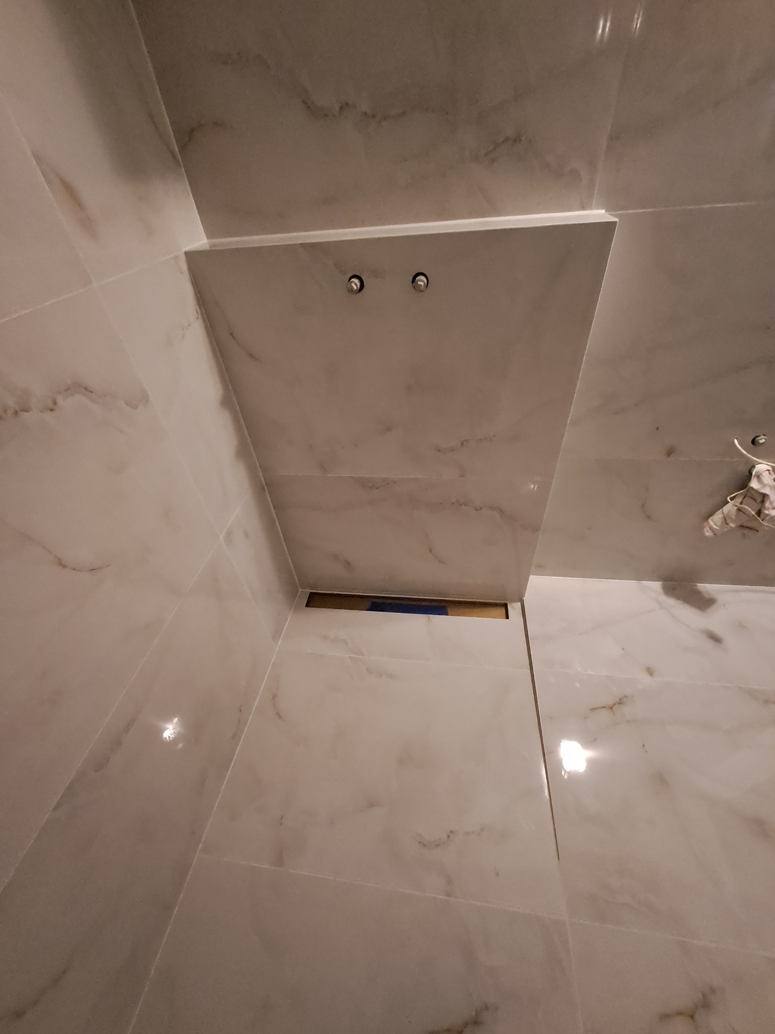 Wykończona łazienka z marmurowymi płytkami, widoczne dwa punkty świetlne w suficie. Ujęcie z dołu, podkreślające precyzję ułożenia płytek i estetykę wykończenia.