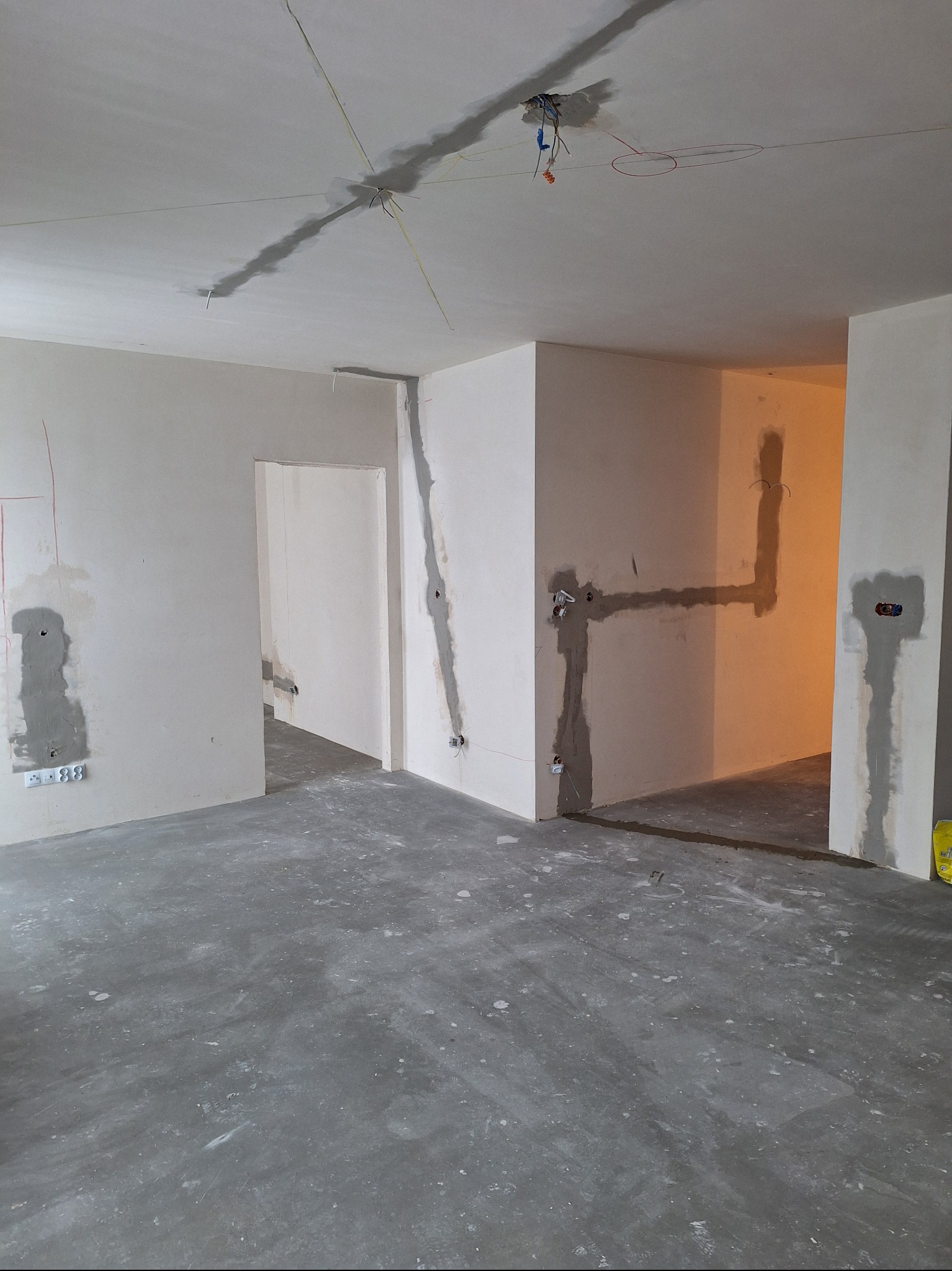 Wnętrze w trakcie prac wykończeniowych: ściany z widocznymi przewodami elektrycznymi i instalacją, częściowo pokryte szpachlą, surowy beton na podłodze.