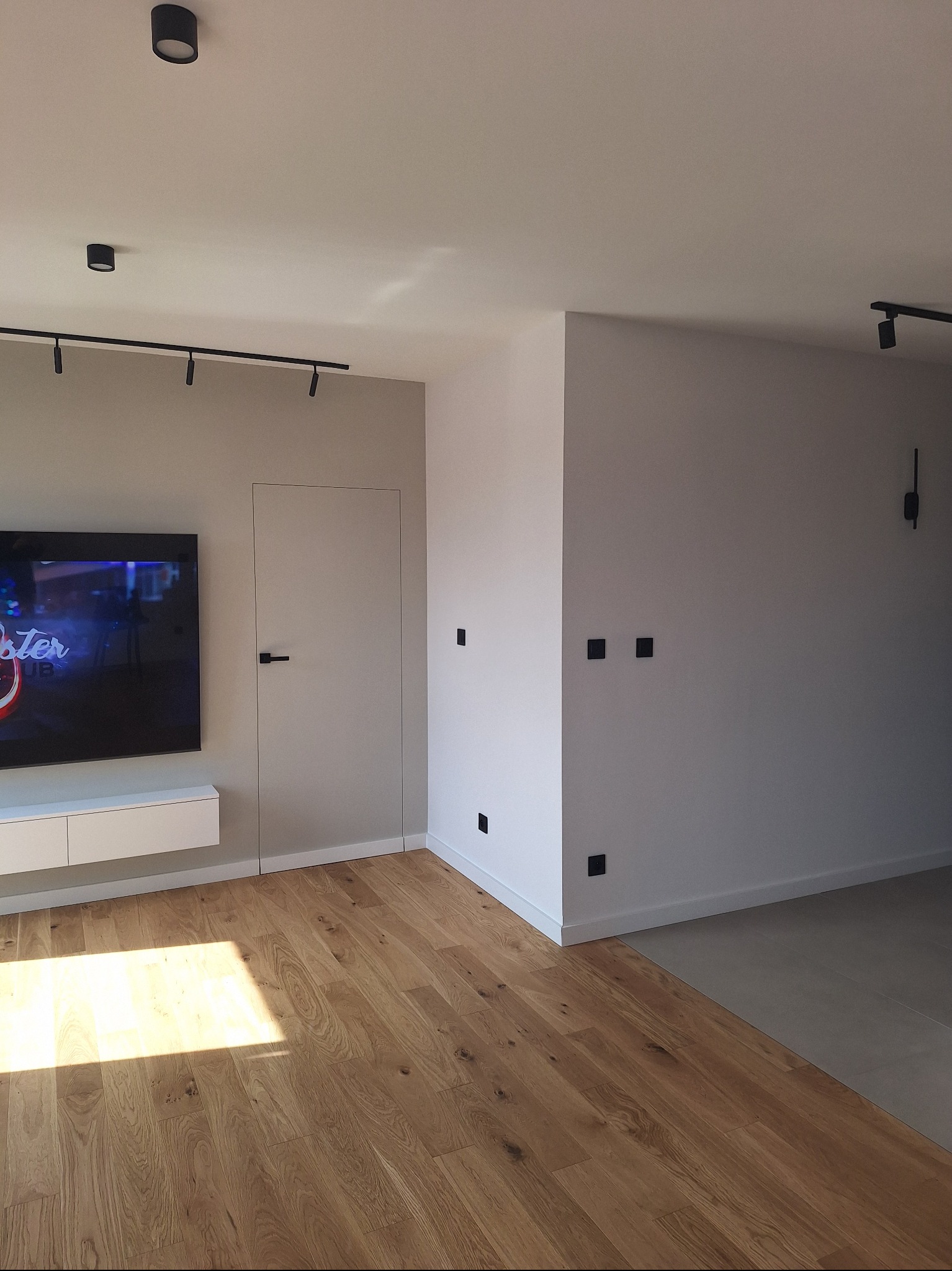 Minimalistyczne wnętrze: drewniana podłoga, gładkie ściany w odcieniach bieli i szarości, ukryte drzwi i nowoczesne oświetlenie punktowe. Nowoczesny design.