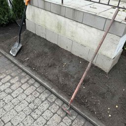 Usługi ogrodnicze Hubert Solarz - Przygotowany teren pod nasadzenia: gleba spulchniona, widoczna łopata z pomarańczowym uchwytem i grabie. Kostka brukowa obok rabaty.