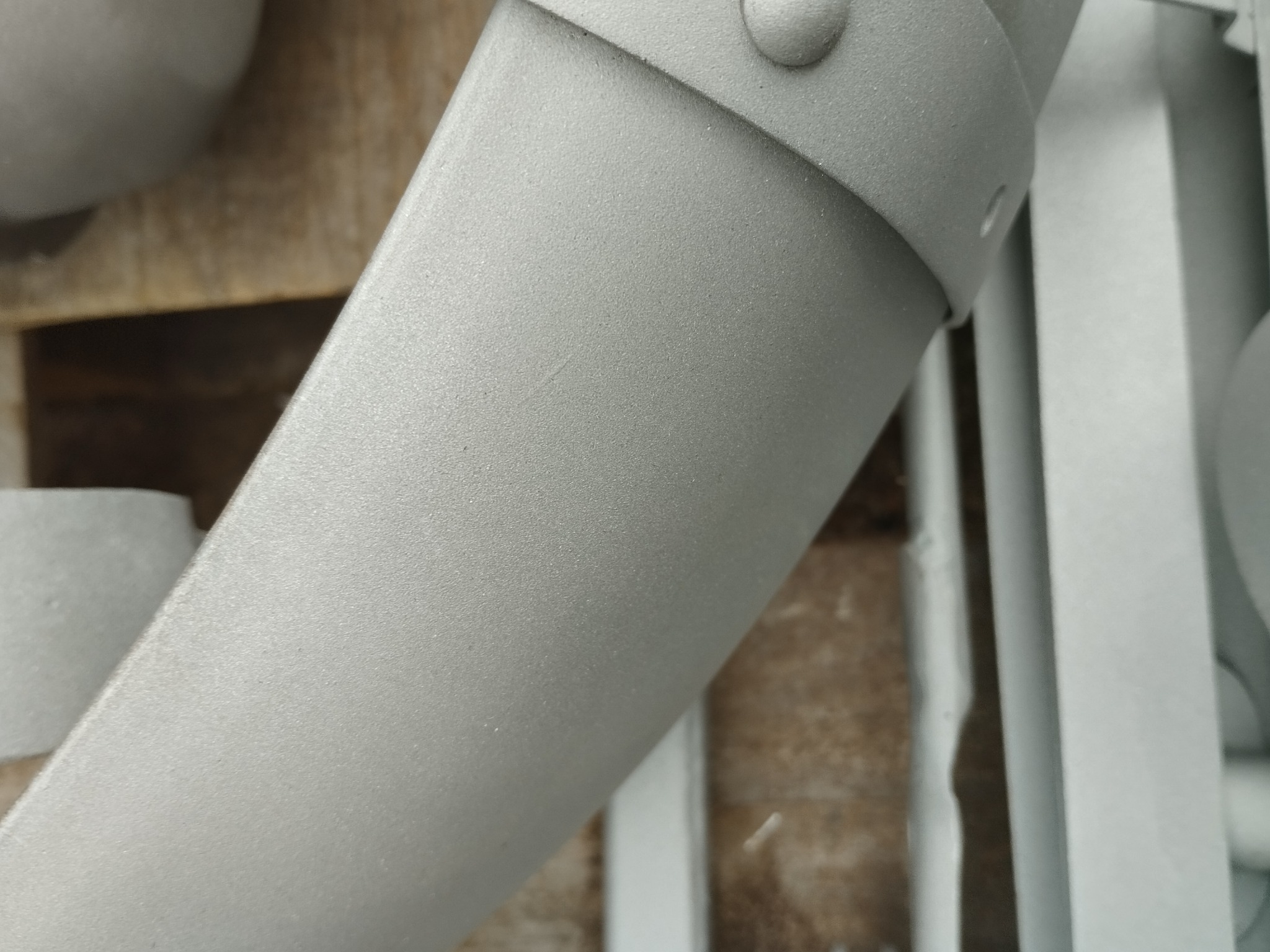 Metalowy element ogrodzenia po obróbce, pokryty jednolitą, szarą powłoką. Widoczne nity i elementy konstrukcyjne. Powierzchnia matowa, jednolita kolorystycznie.