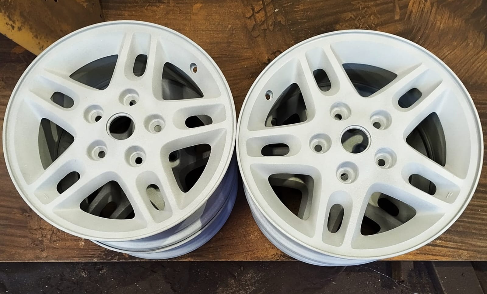 Dwa stosy białych felg aluminiowych po obróbce, leżące na ciemnej powierzchni. Widoczne detale konstrukcji i świeża, matowa powłoka.