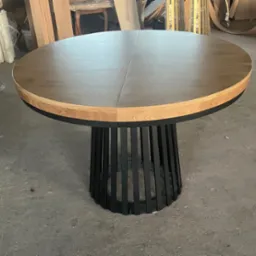 Okrągły st&oacute;ł z drewnianym blatem i czarną, metalową podstawą w kształcie klatki. Blat składa się z dw&oacute;ch części, widoczne łączenie na środku.