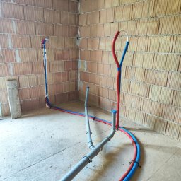 Tomasz Gorlowski - Surowy mur z instalacją wodną i kanalizacyjną, rury w kolorach niebieskim i czerwonym. Widoczne łączenia i mocowania. Stan surowy, przed wykończeniem.