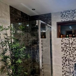 Jankowski - Nowoczesna łazienka z kabiną prysznicową, wykończona płytkami w odcieniach szarości i brązu. Dekoracyjne płytki geometryczne i bambus dodają charakteru.