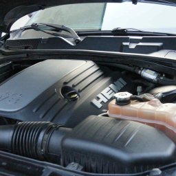 Mobilny Urban Shine Detailing - Otwarta maska czarnego samochodu z widocznym silnikiem V8 Hemi, zbiornikiem płynu chłodniczego i filtrem powietrza. Widoczne elementy instalacji elektrycznej i węże.