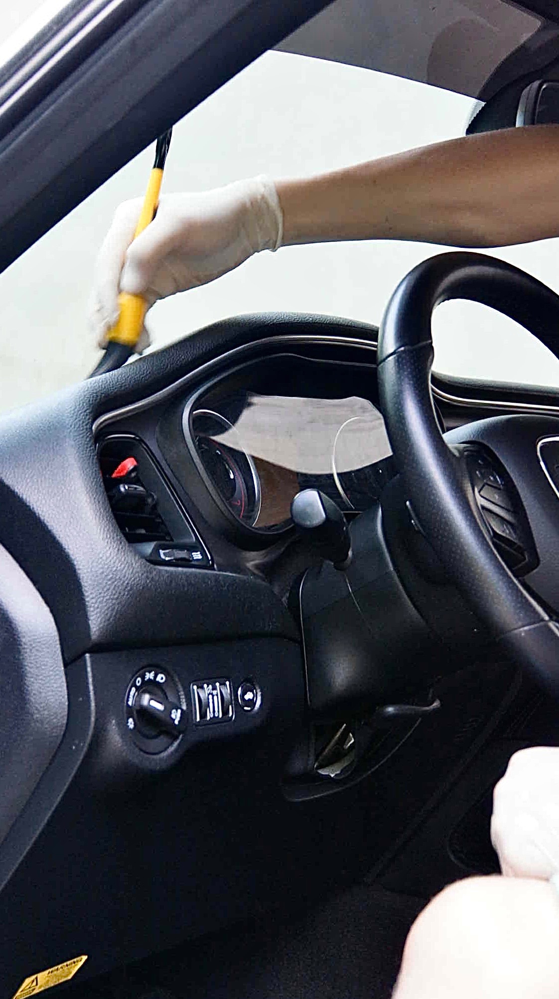 Czyszczenie deski rozdzielczej samochodu pędzlem przez osobę w rękawiczkach, widoczne detale wnętrza pojazdu.