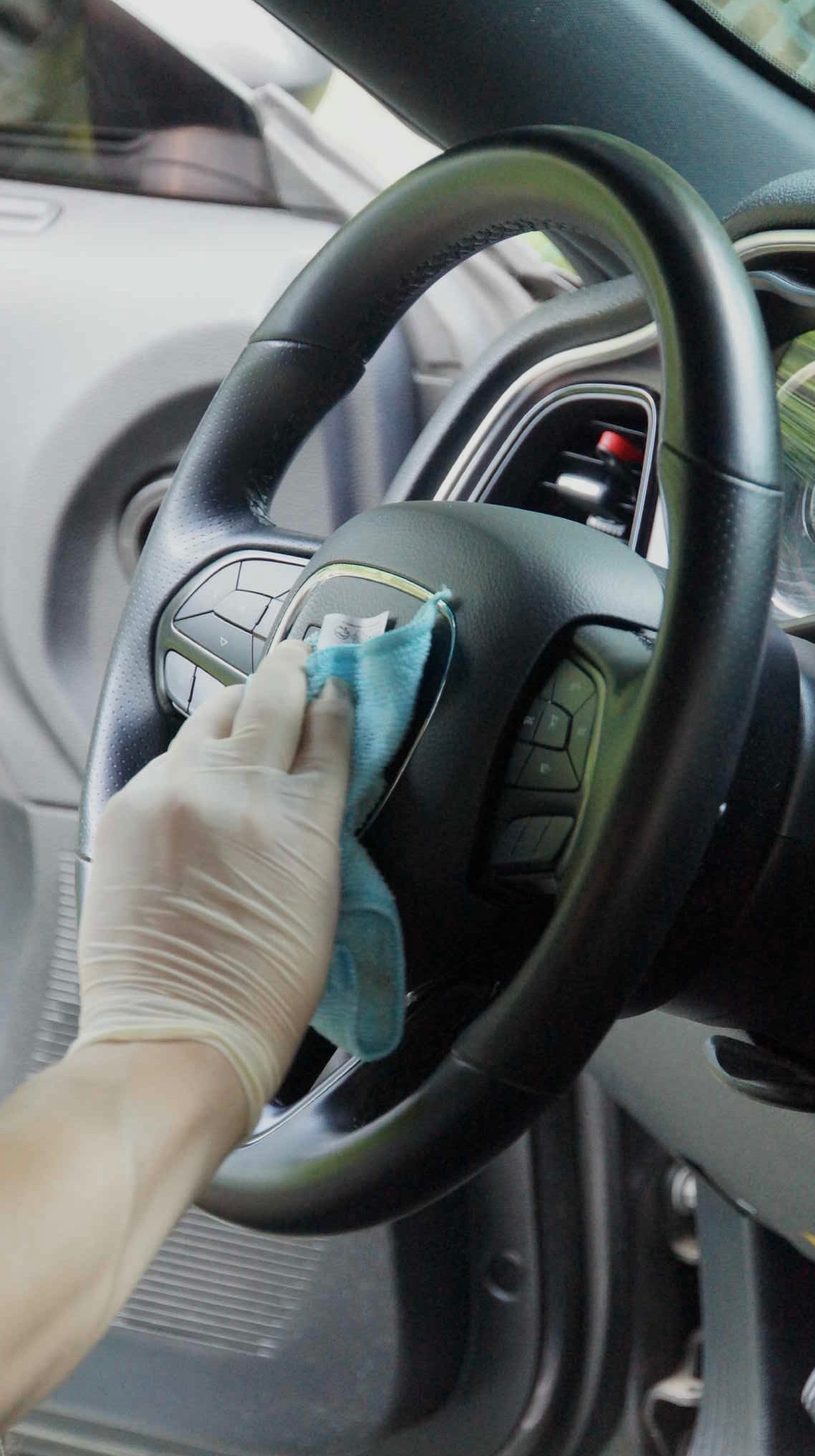 Czyszczenie kierownicy samochodu miękką, błękitną ściereczką przez osobę w lateksowej rękawiczce, wnętrze pojazdu, detale deski rozdzielczej.