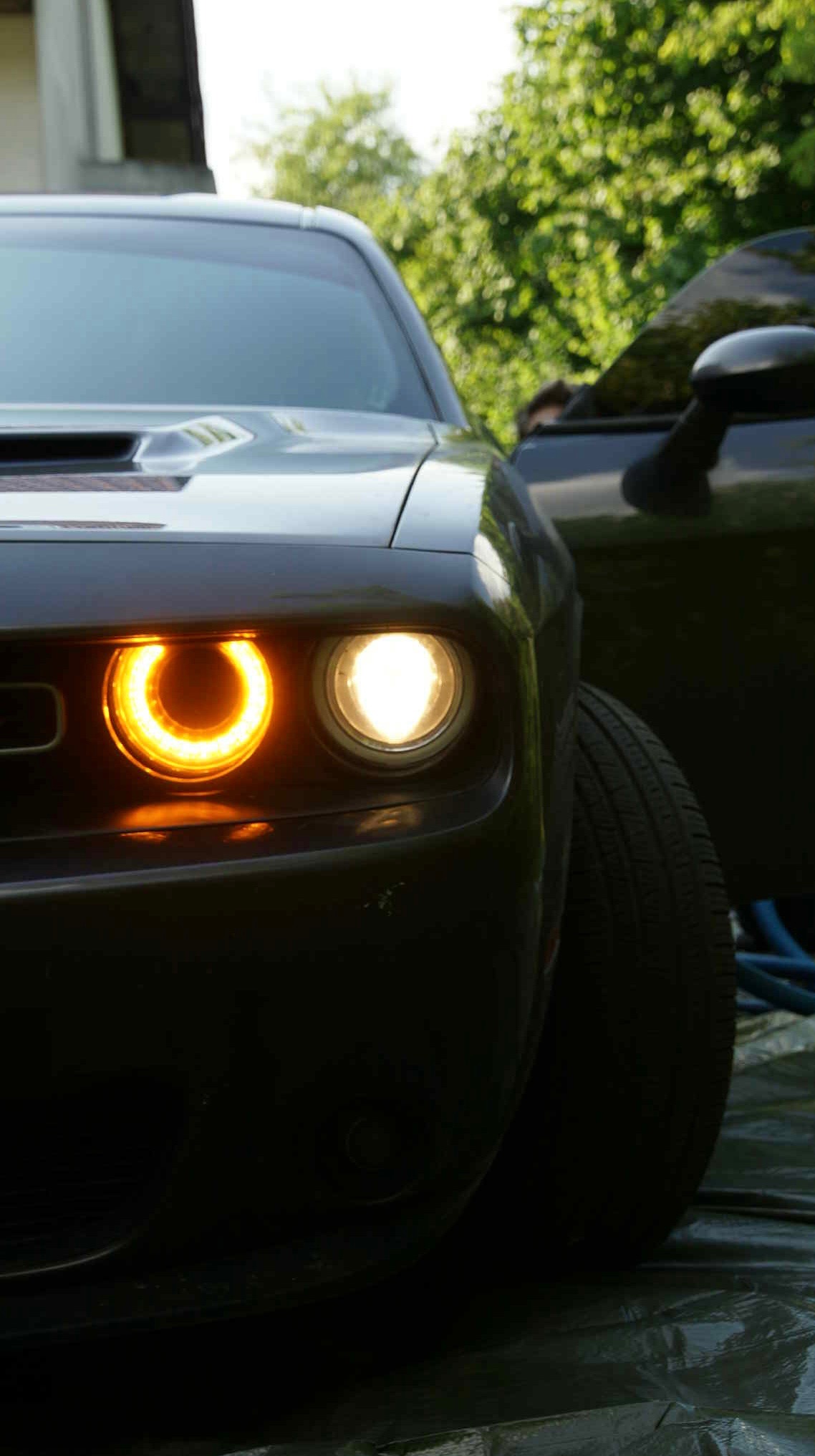 Czarny samochód z włączonymi światłami LED, widok z przodu, z otwartymi drzwiami w tle. Oświetlenie podkreśla detale karoserii.