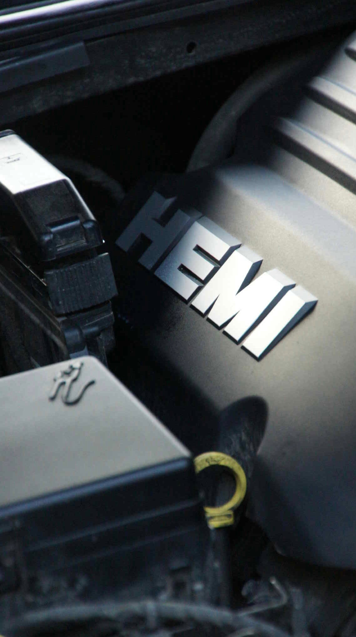 Silnik samochodu z chromowanym napisem 'HEMI', widoczny wlew oleju i elementy osprzętu w ciemnych barwach. Detal pod maską auta.