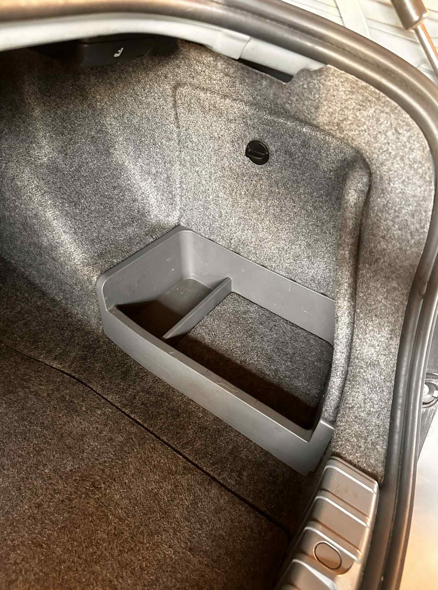 Szare wnętrze bagażnika samochodowego z wbudowanym, plastikowym organizerem. Wykładzina z filcu. Widoczny fragment karoserii i elementy mocujące.