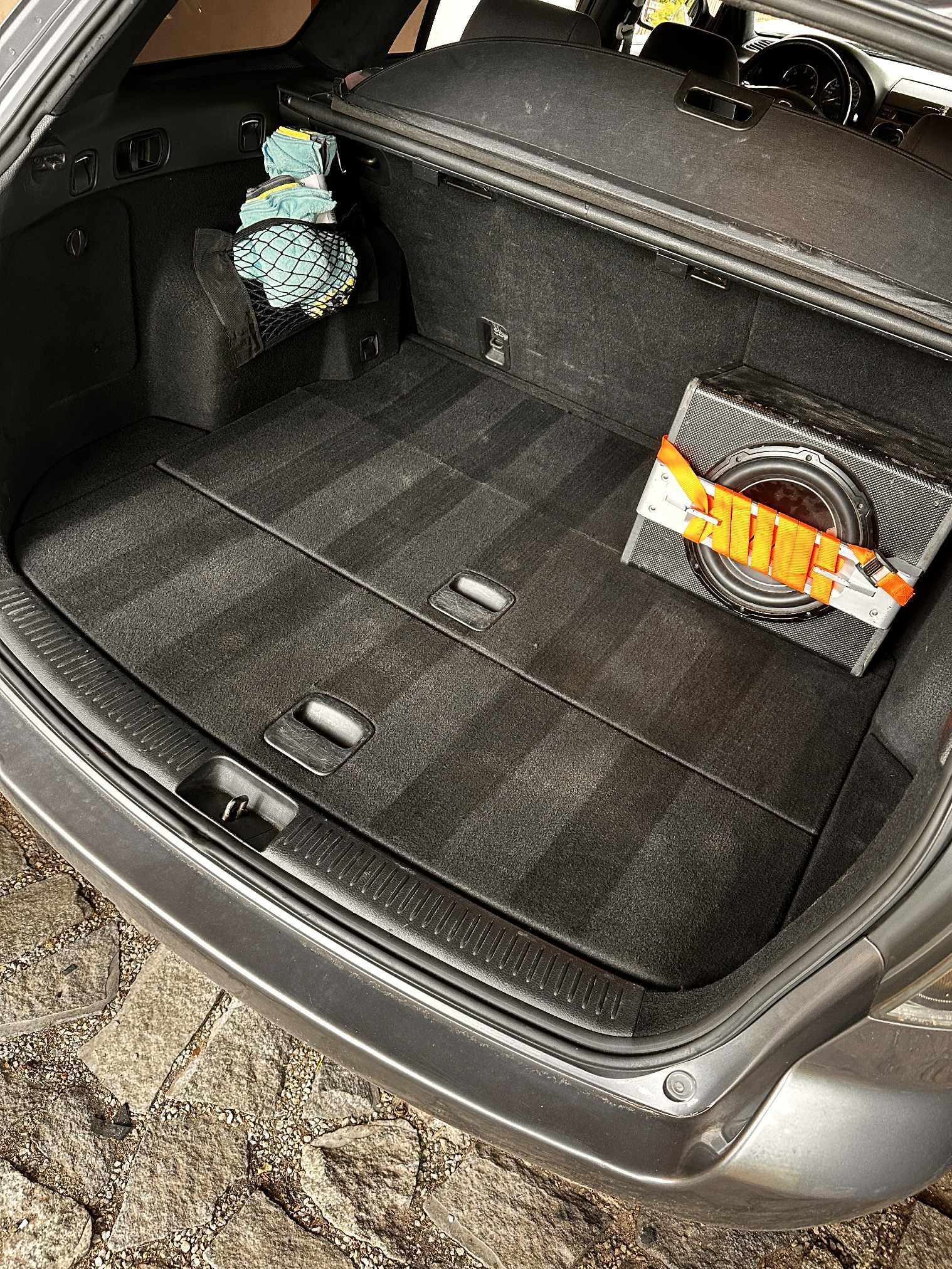 Bagażnik auta po czyszczeniu tapicerki. Widoczne ślady po odkurzaczu i umytych elementach. W tle subwoofer i siatka z akcesoriami.