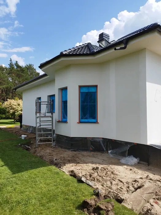 Elewacja domu jednorodzinnego w Lubniewicach po tynkowaniu, okna zabezpieczone folią, widoczne rusztowanie i przygotowany teren wokół budynku.